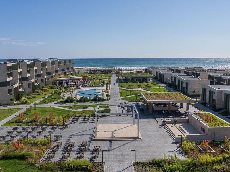 Modern hotelcomplex met zwembad en uitzicht op zee onder heldere lucht.