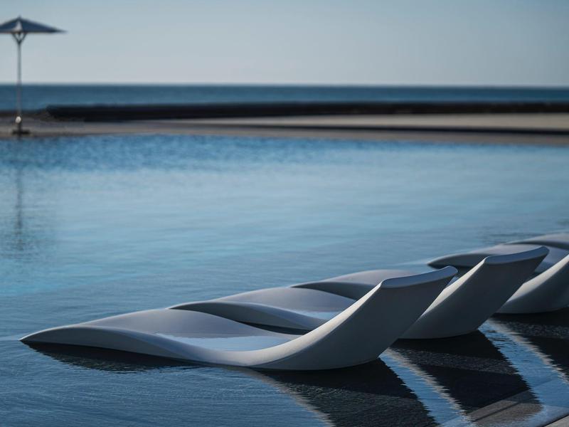 Moderne ligstoelen aan de rand van een infinity-zwembad met uitzicht op zee en strakke lijnen.