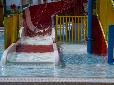 Rote Wasserrutsche mündet in ein flaches Schwimmbecken mit buntem Geländer.