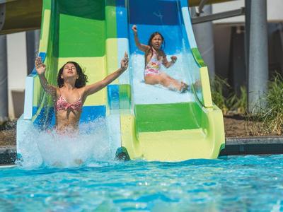 Zwei Frauen rutschen auf bunten Wasserrutschen in einen Pool.