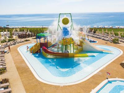 Bunter Wasserspielplatz mit Rutschen und großen Wassereimern neben Hotels an der Küste.