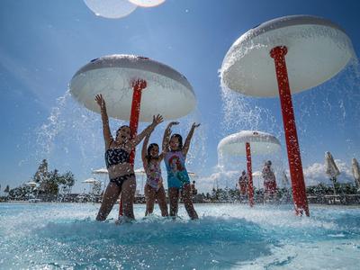 Des enfants jouent sous de grands jets d'eau en forme de champignons dans un parc aquatique par une journée ensoleillée.