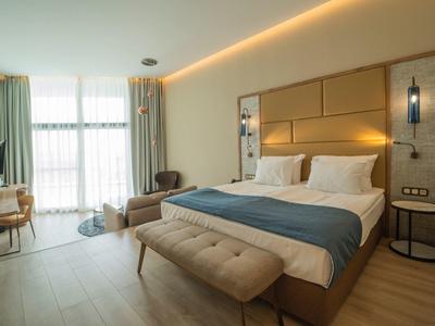 Modernes Hotelzimmer mit großem Bett, Sitzbereich und viel Tageslicht durch große Fenster.