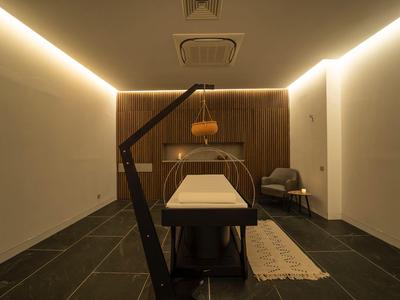 Modern eingerichteter, gedämpft beleuchteter Wellnessraum mit Massageliege und einem Sessel in ruhiger Atmosphäre.