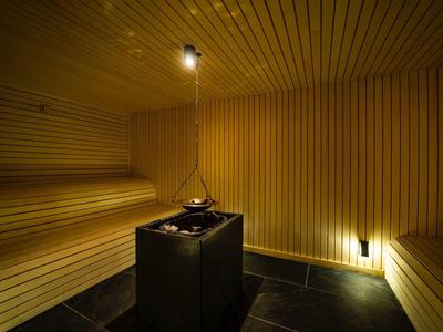 Holzsauna mit warmem Licht, Holzbänken und einem zentralen Ofen für Aufgusssteine.