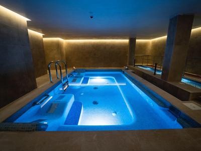 Modern beleuchteter Innenpool mit Whirlpool-Bereich in einem luxuriösen Spa-Bereich.