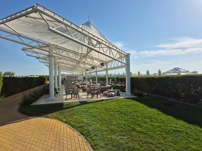 Moderner Außenbereich mit gedecktem Sitzbereich und gepflegtem Rasen unter blauem Himmel.