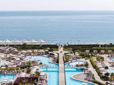 Blick auf Resort mit Pools, Sonnenliegen und Meer im Hintergrund bei klarem Wetter.
