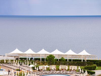 Blick auf einen Poolbereich mit Sonnenschirmen vor ruhigem Meer und blauem Himmel.