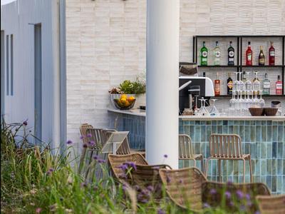 Moderner Außenbereich mit Bar, Stühlen und grüner Bepflanzung an einem sonnigen Tag.