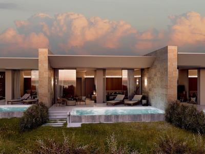 Moderner Hotelkomplex mit privaten Pools und Sitzbereichen vor einem bewölkten Himmel bei Sonnenuntergang.