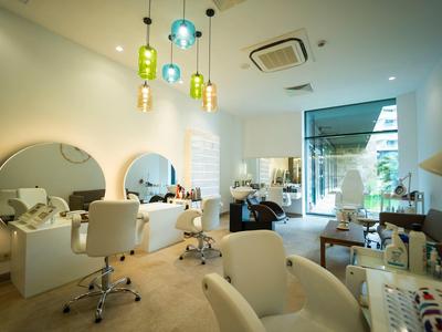 Heller Friseursalon mit runden Spiegeln, weißen Stühlen und bunten Hängelampen.