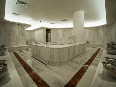 Moderner Hamam mit Marmorwänden, Sitzbereichen und gedeckter Beleuchtung