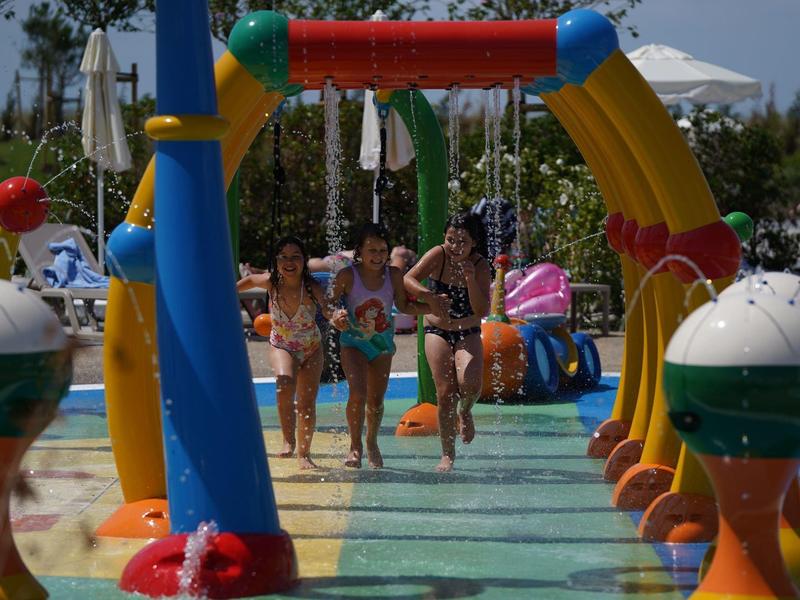 Kinder spielen unter Wasserwasserfontänen im Schwimmbad bei sonnigem Wetter.
