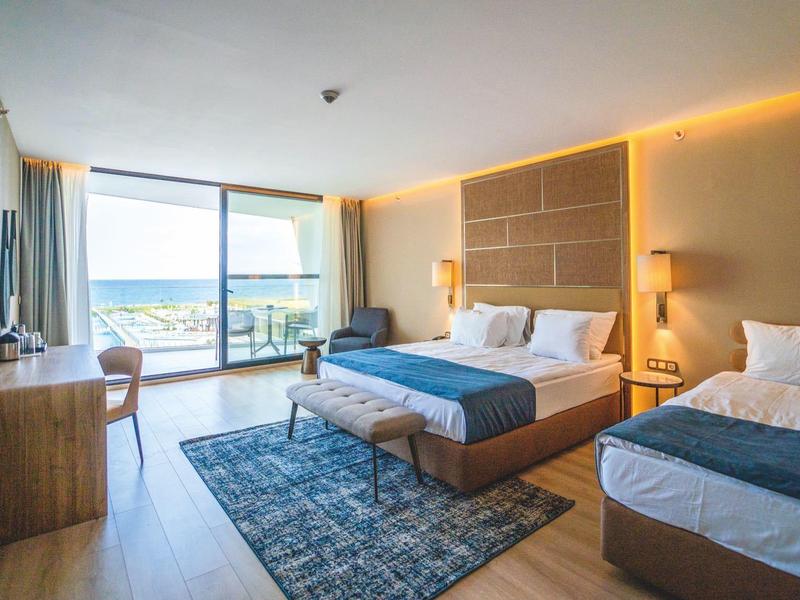 Modernes Hotelzimmer mit zwei Einzelbetten, Schreibtisch, Fernseher und Balkon mit Meerblick.