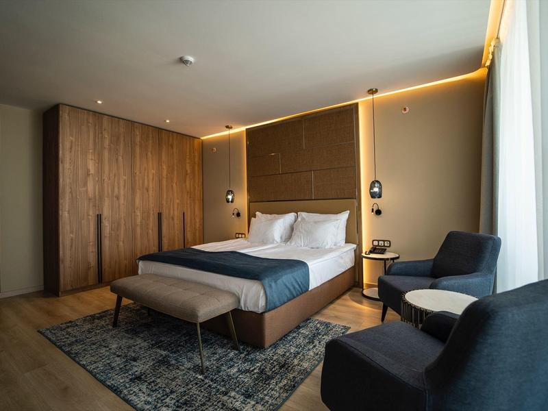 Modern eingerichtetes Hotelzimmer mit Doppelbett, Sitzbereich und großen Fenstern.