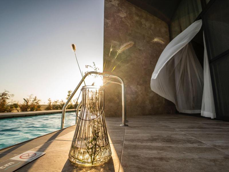 Sonnenuntergang am Hotelpool mit einem Glas und wehender Gardine auf der Terrasse.