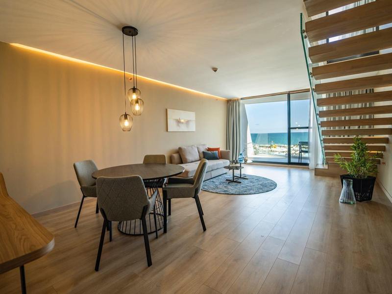 Heller Wohnbereich mit Holzboden, moderner Treppe und Blick aufs Meer durch große Fenster.