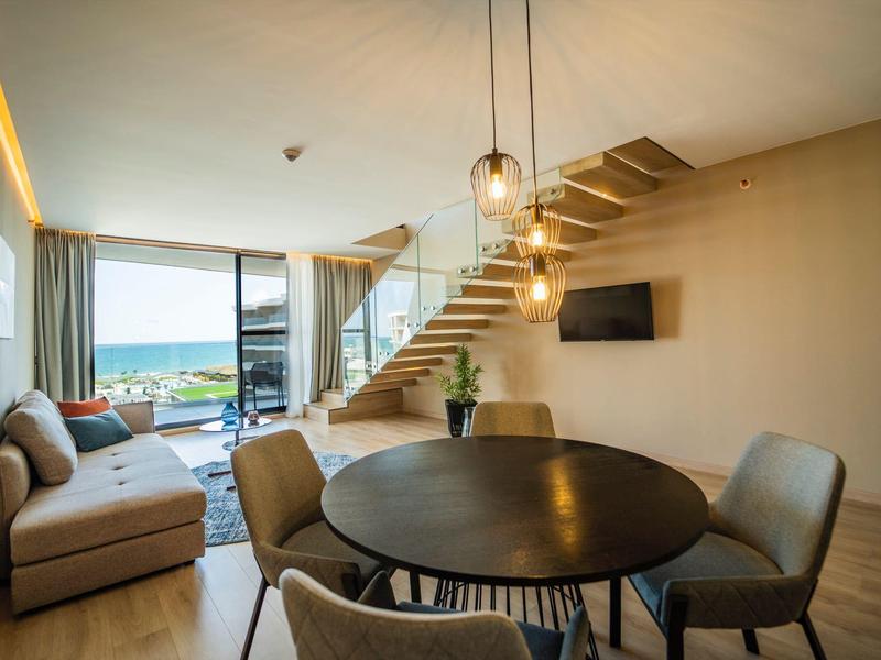 Moderner Wohnbereich mit Sofa, runden Esstisch, Treppe und Blick auf Balkonaussicht.