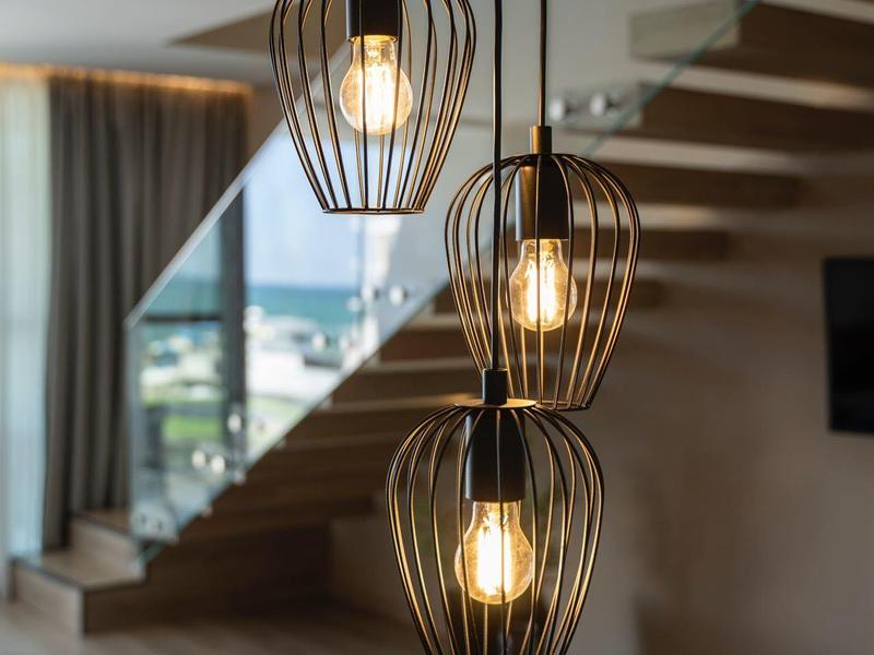 Drei hängende Lampen mit Glühbirnen vor einer Treppe und großem Fenster