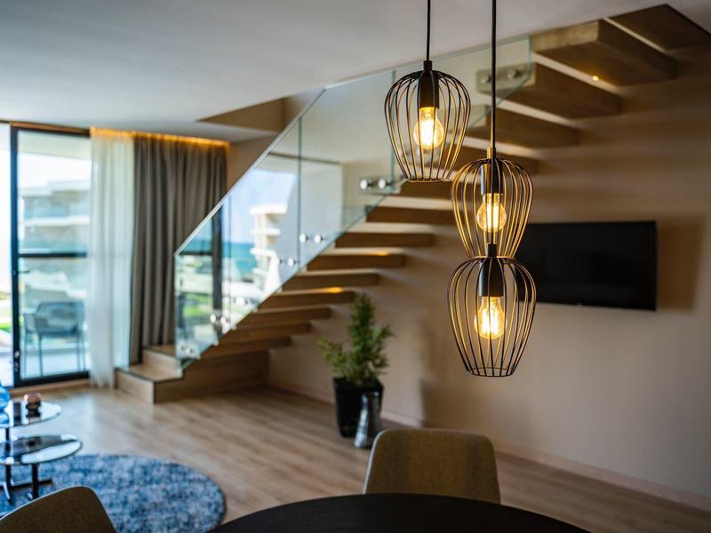 Moderner Wohnbereich mit hölzernem Treppenaufgang, Hängeleuchten und großem Fenster mit Meerblick.