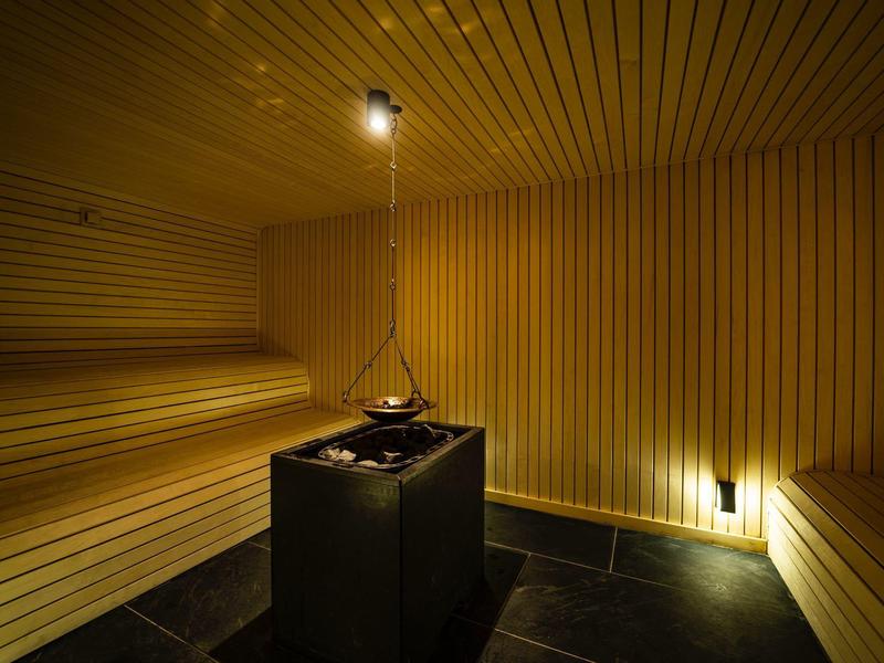 Holzsauna mit warmem Licht, Holzbänken und einem zentralen Ofen für Aufgusssteine.