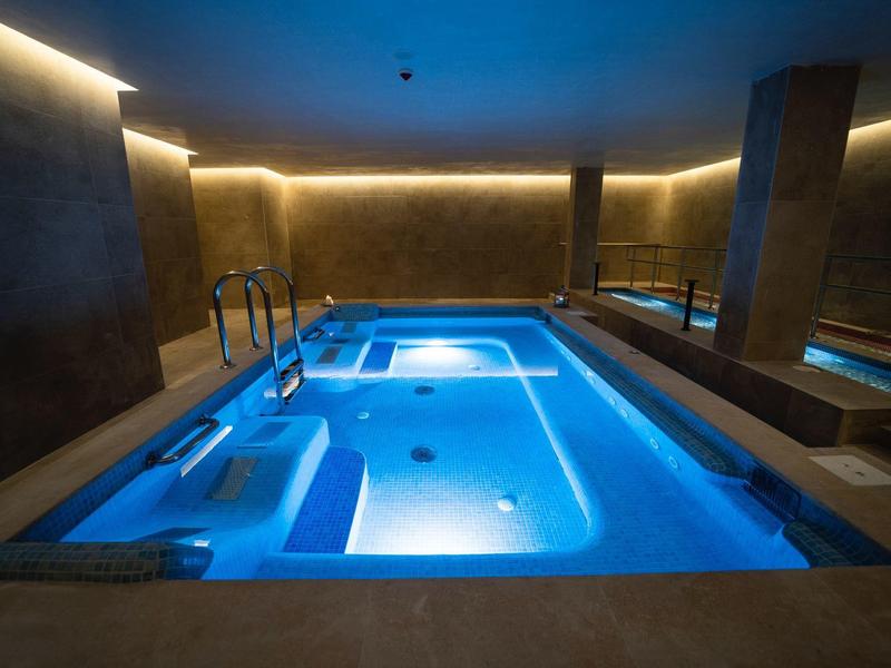 Modern beleuchteter Innenpool mit Whirlpool-Bereich in einem luxuriösen Spa-Bereich.