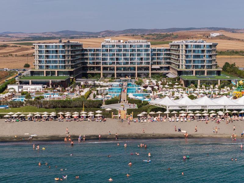 Großes Hotel mit Pool und Liegestühlen am Strand in einer ländlichen Gegend.