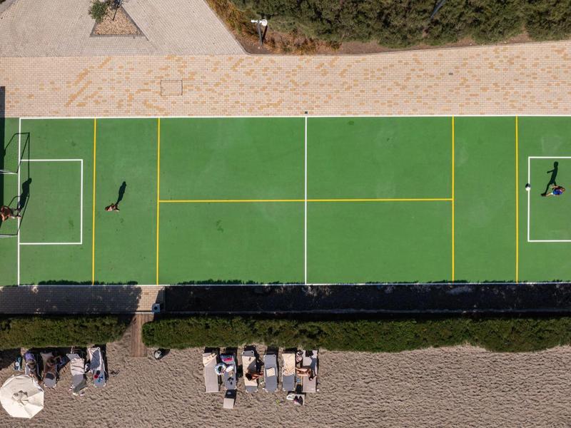 Vogelperspektive eines grünen Sportplatzes mit zwei Personen und umliegenden Sitzbereichen.