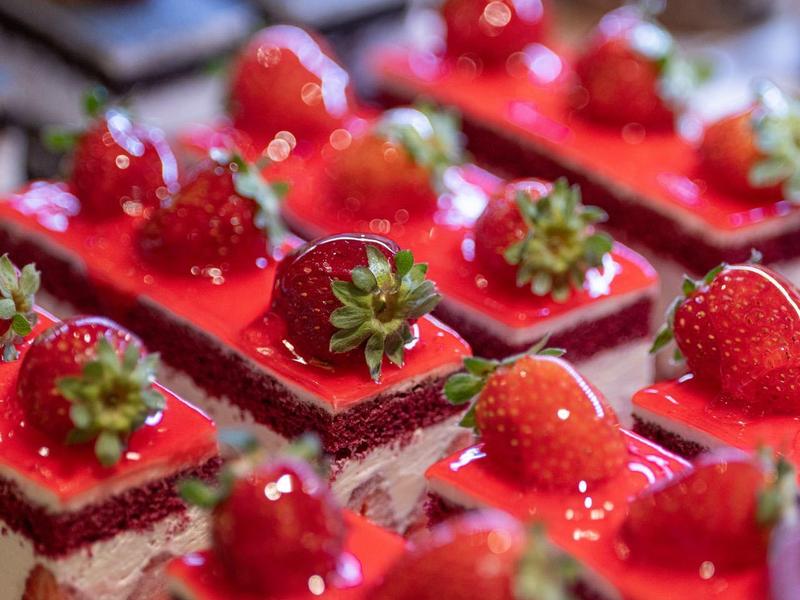 Nahaufnahme von quadratischen Erdbeertortenstücken mit roter Glasur und frischen Erdbeeren.