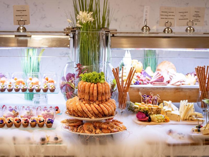 Buffet mit verschiedenen Backwaren und Obst, dekoriert mit Blumen in einem Hotelrestaurant.