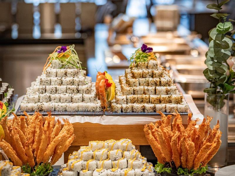 Buffet mit Sushi, Garnelen und Saucen in einem eleganten Restaurant mit Blick auf ein Fenster.