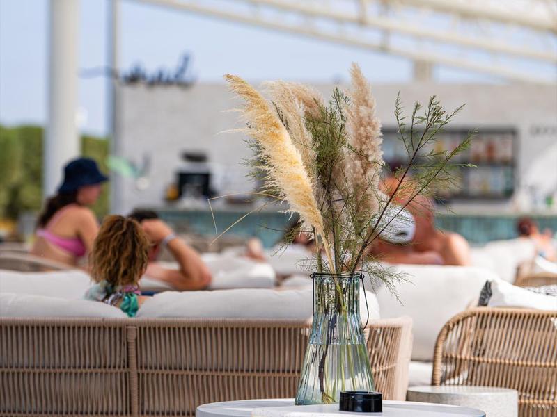 Vase mit getrocknetem Pampasgras auf einem weißen Tisch vor Lounge-Möbeln in einem hellen Hotelbereich.