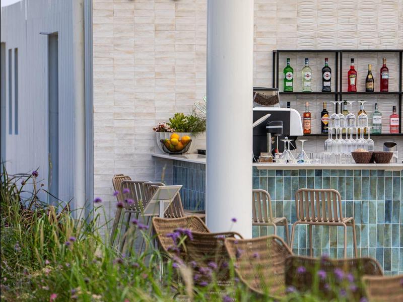 Moderner Außenbereich mit Bar, Stühlen und grüner Bepflanzung an einem sonnigen Tag.