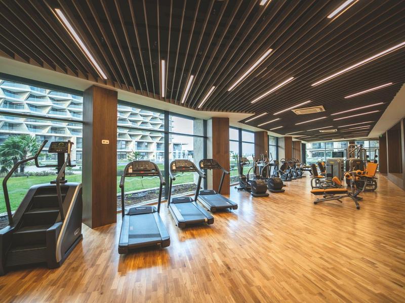 Großer moderner Fitnessraum mit Laufbändern, Kraftgeräten und großen Fenstern mit Ausblick.