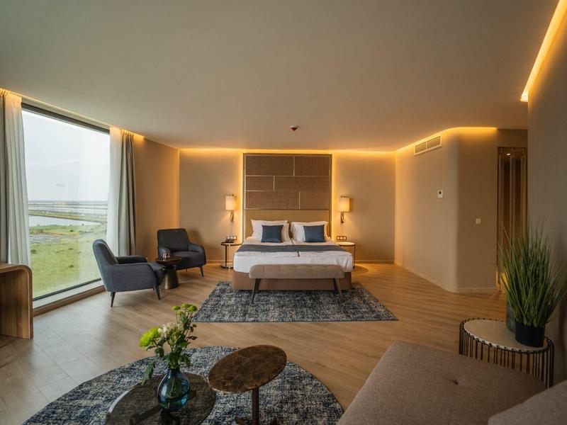 Modern eingerichtetes Hotelzimmer mit großem Bett, Sesseln und Panoramafenster mit Ausblick.