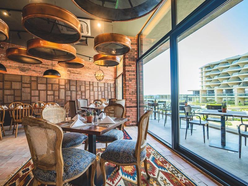 Innenraum eines stilvollen Restaurants mit Vintage-Möbeln und großem Fenster zur Terrasse.