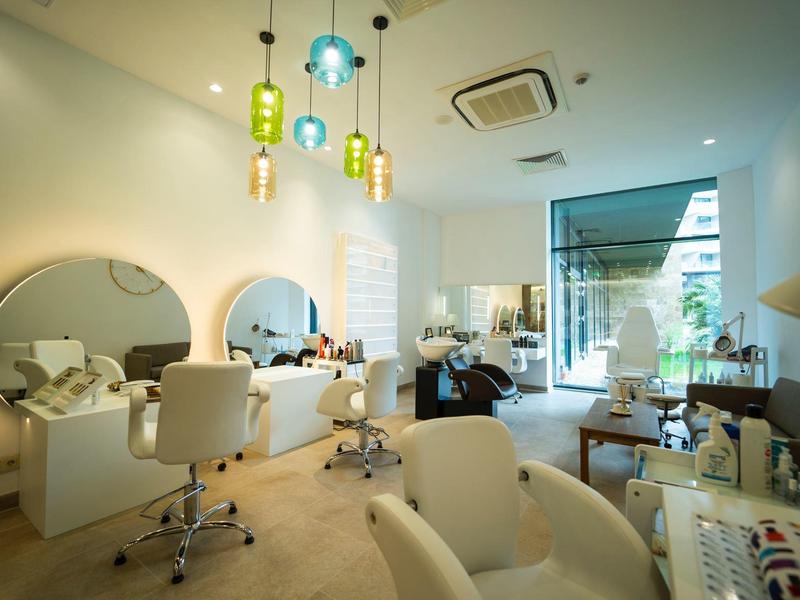 Heller Friseursalon mit runden Spiegeln, weißen Stühlen und bunten Hängelampen.