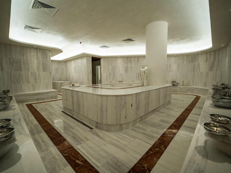 Moderner Hamam mit Marmorwänden, Sitzbereichen und gedeckter Beleuchtung
