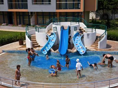 Děti si hrají v mělkém bazénu s tobogány před hotelem.