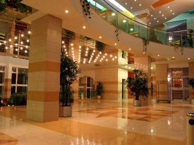 Großer heller Innenraum mit Säulen, Pflanzen und gläsernem Geländer im Einkaufszentrum.