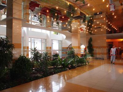 Bright hotel lobby with plants, staircase, and decorative ceiling lights.
