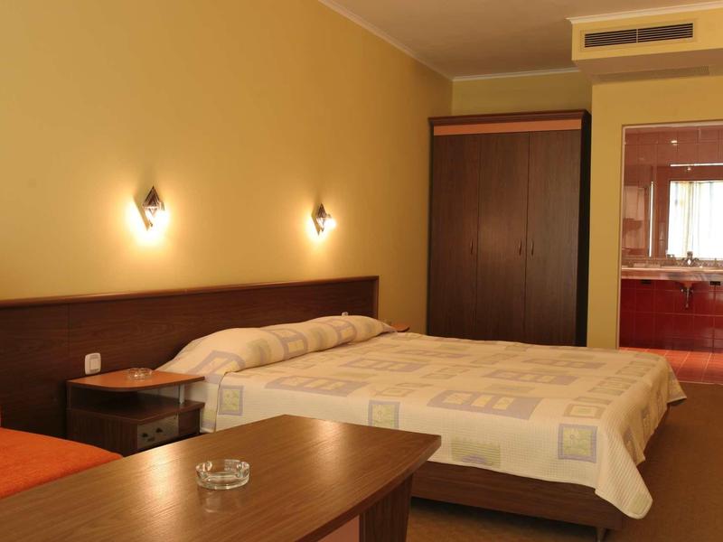 Bedroom with double bed, nightstand, wardrobe, and orange chair in a hotel room.