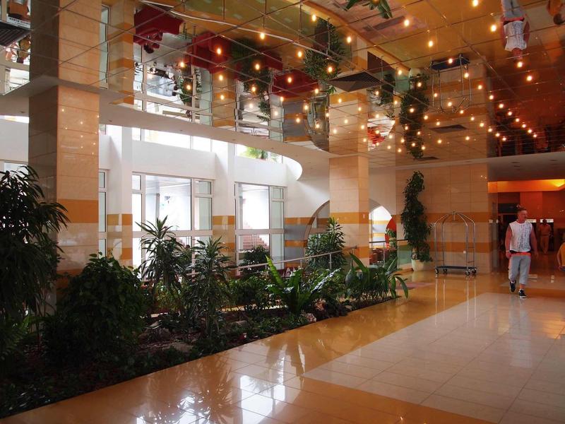Bright hotel lobby with plants, staircase, and decorative ceiling lights.
