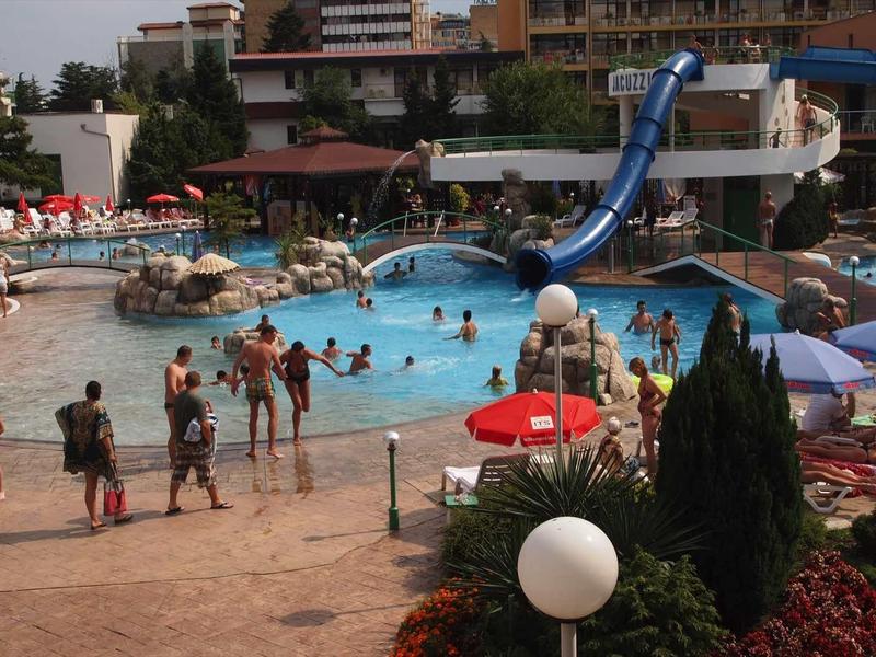 Busy hotel pool with waterslide, umbrellas, and guests on loungers and in the water.