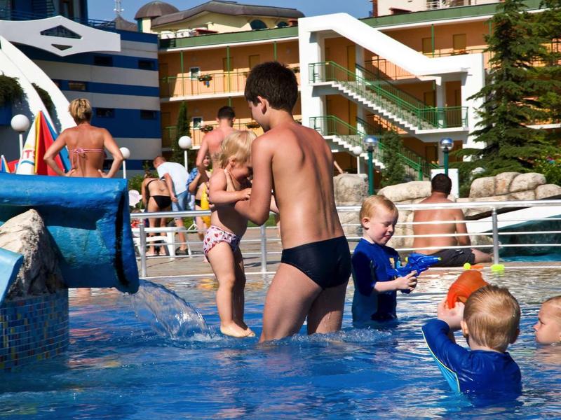 Children playing in hotel pool with water slides and multi-level buildings in the background.