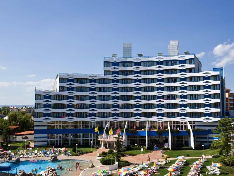 Modern hotel with distinctive blue wave facade and pool area with umbrellas and loungers.