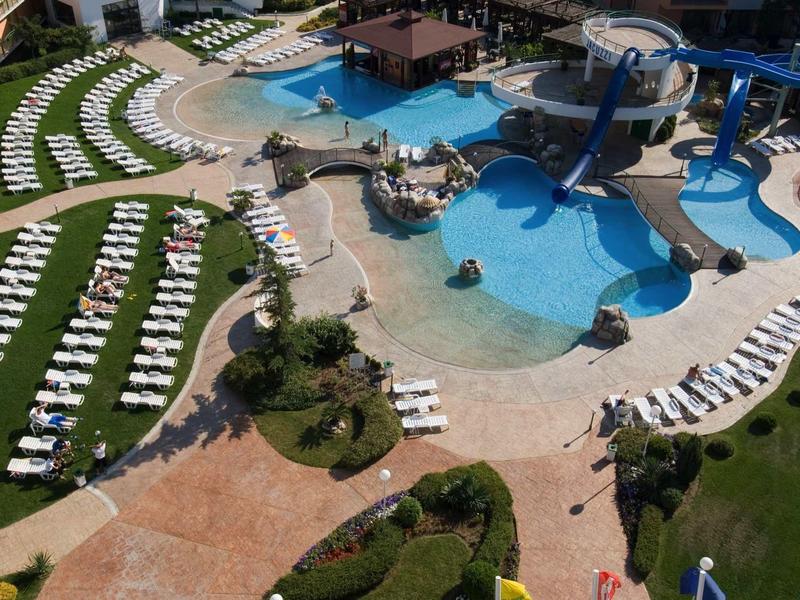 Large hotel pool with water slides, surrounding lounge chairs, and well-maintained lawns.