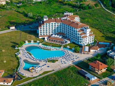 Grande hotel con piscina curva e lettini circondati da aree verdi.