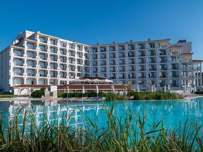 Hotel moderno con molte balconi e grande piscina all'aperto sotto un cielo azzurro.